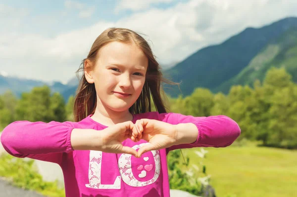 Outdoor portrait of a cute little girl making heart sign with her hands — Stock Photo, Image