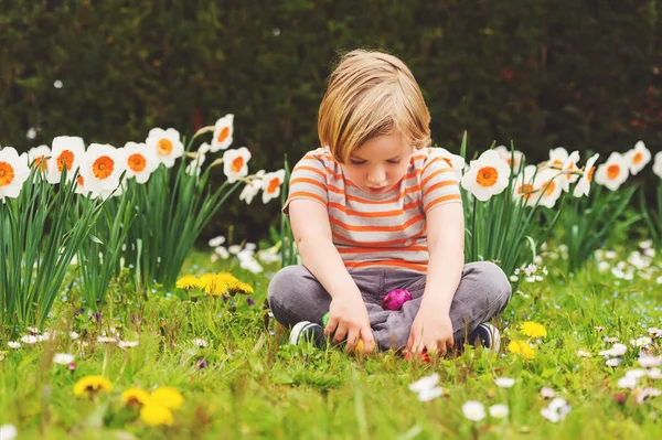 Adorable little blond boy playing with colorful easter eggs in the park, egg hunt — Stock Photo, Image