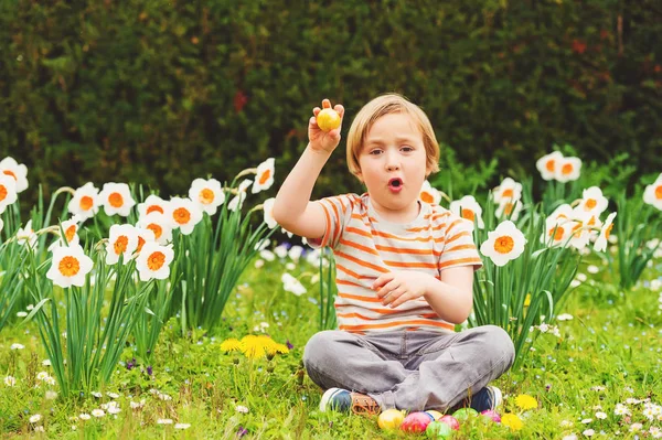 Menino louro adorável brincando com ovos coloridos de páscoa no parque, caça aos ovos — Fotografia de Stock