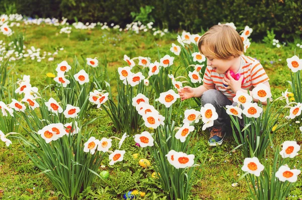 Entzückender kleiner blonder Junge spielt mit bunten Ostereiern im Park, Eiersuche — Stockfoto