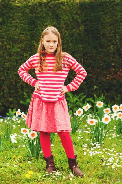 Cute little girl of 7-8 years old playing in the spring park between daffodils flowers, wearing stripe pullover, red skirt and tights, brown leather boots — Stock Photo, Image