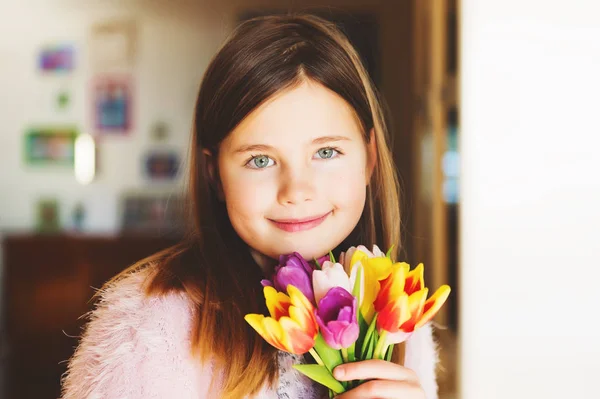 Очаровательная улыбающаяся маленькая девочка с голубыми глазами, держащая маленький букет ярких свежих тюльпанов — стоковое фото
