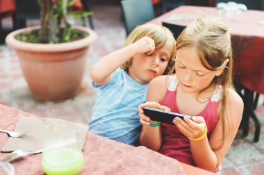 Restoranda yemek sipariş beklerken telefonda elektronik oyunlar oynayan iki çocuklar