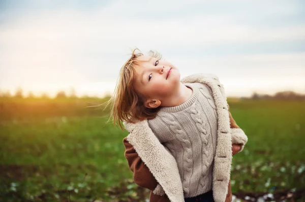 Criança adorável brincando ao ar livre ao pôr do sol, vestindo casaco bege quente e pulôver — Fotografia de Stock