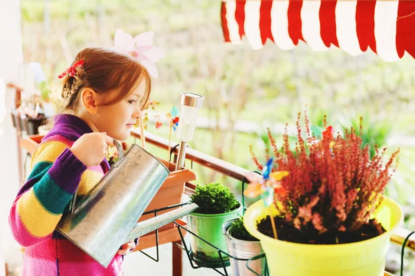 Adorable little girl watering plants on the balcony on a nice sunny day — Stock Photo, Image