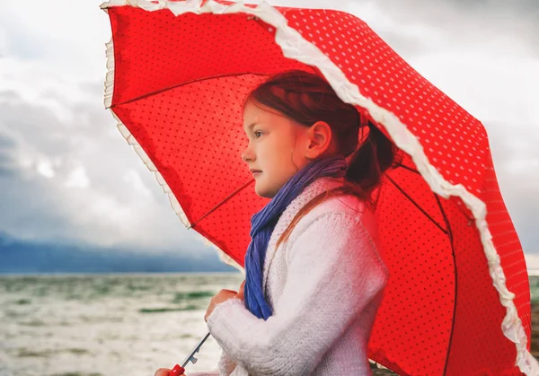 Little girl with big red umbrella next to lake on a very cold day — Stock Photo, Image