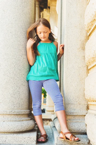 Egy aranyos kis lány visel zöld tetején, szabadban közlekednek a város nyári portréja — Stock Fotó