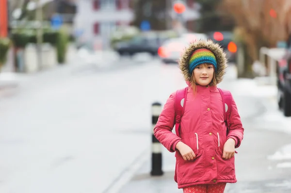 Liten skolflicka med ryggsäck i vinter, bär varma röda jacka — Stockfoto