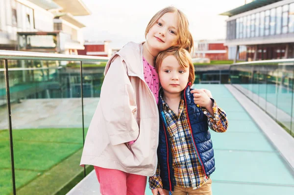 Két aranyos gyerekek, a kis testvér és a nagy testvér, a fiú és a lány egy városban, tavaszi kabátok visel szabadtéri portréja — Stock Fotó