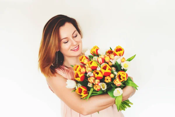 Joyeux jeune femme aux cheveux rouges tenant un gros bouquet de tulipes rouges jaunes debout sur fond blanc — Photo