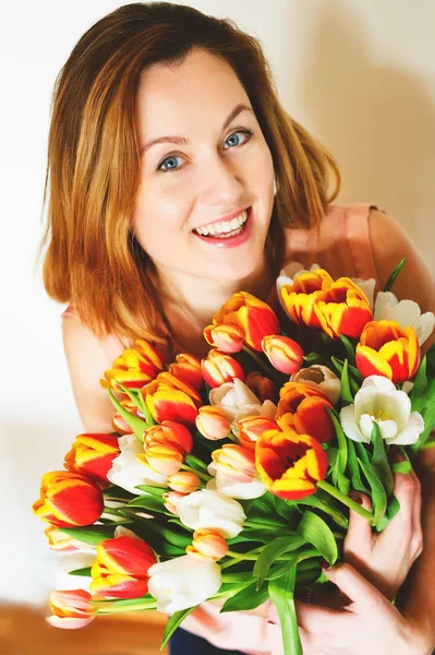 Joyeux jeune femme aux cheveux rouges tenant un gros bouquet de tulipes rouges jaunes debout sur fond blanc — Photo