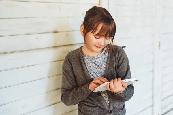 Carino bambina che gioca con tablet pc, in piedi contro sfondo di legno bianco — Foto Stock