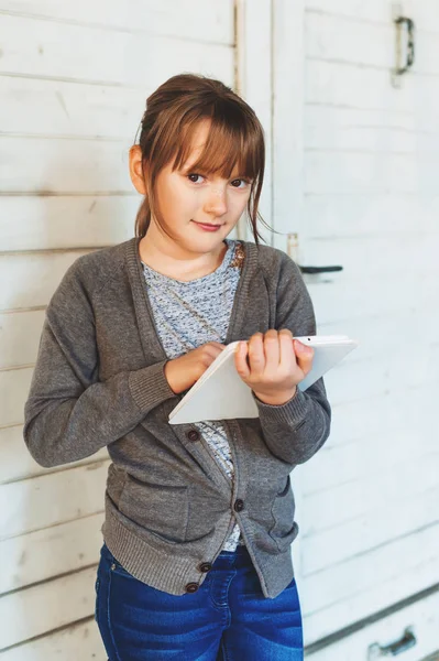 Cute little girl playing with tablet pc, standing against white wooden background — Stock Photo, Image