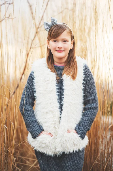 Outdoor portrait of cute 8-9 year old girl wearing grey pullover and white faux fur gilet — Stock Photo, Image