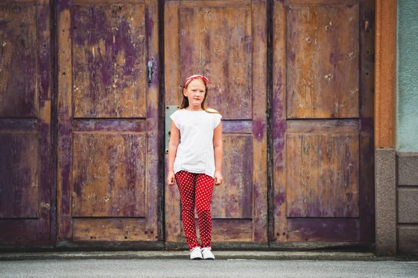 Outdoor fashion portrait of 8-9 year old girl walking down the street, wearing polkadot trousers and white tee shirt, toned image — Stock Photo, Image