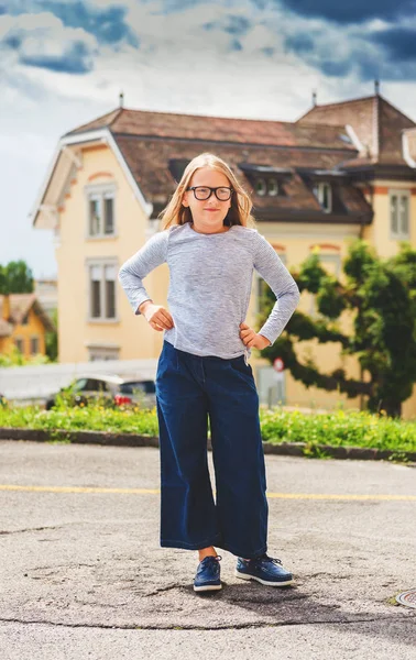 Retrato divertido al aire libre de una linda niña de 9-10 años con top azul, culottes de denim y gafas graduadas —  Fotos de Stock