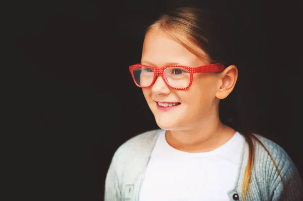 Ritratto di una graziosa bambina in occhiali a pois rossi sullo sfondo nero — Foto Stock