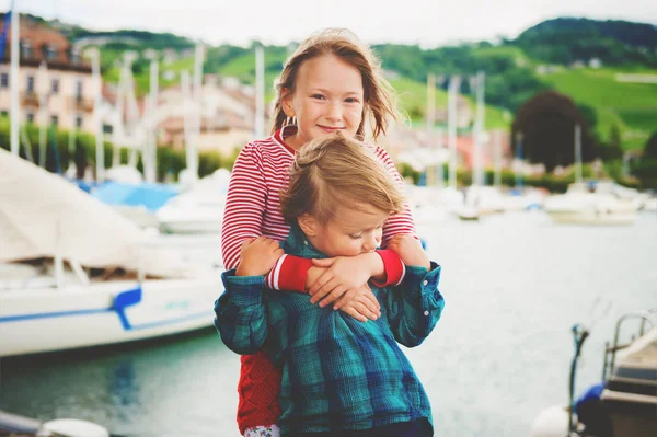 Двое маленьких детей играют вместе на озере Женева в очень ветреный день, обнимая друг друга — стоковое фото
