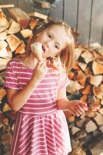 Menina bonito pouco 6 anos comendo sorvete ao ar livre, vestindo vestido de listra rosa, prazeres de verão para crianças — Fotografia de Stock
