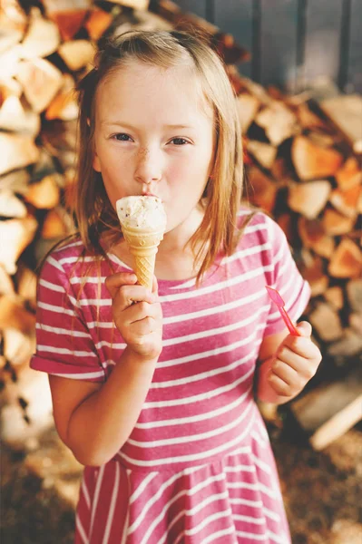 Menina bonito pouco 6 anos comendo sorvete ao ar livre, vestindo vestido de listra rosa, prazeres de verão para crianças — Fotografia de Stock