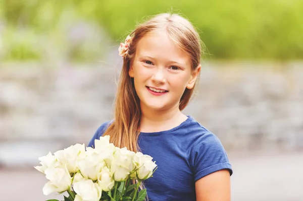 Outdoor portrait of a yong little girl of 9 years old, wearing blue tee shirt, holding fresh bouquet of beautiful white roses — Stock Photo, Image