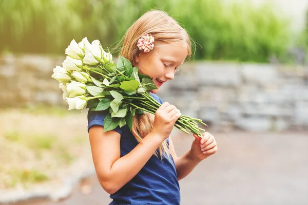 Outdoor portrait of a yong little girl of 9 years old, wearing blue tee shirt, holding fresh bouquet of beautiful white roses — Stock Photo, Image