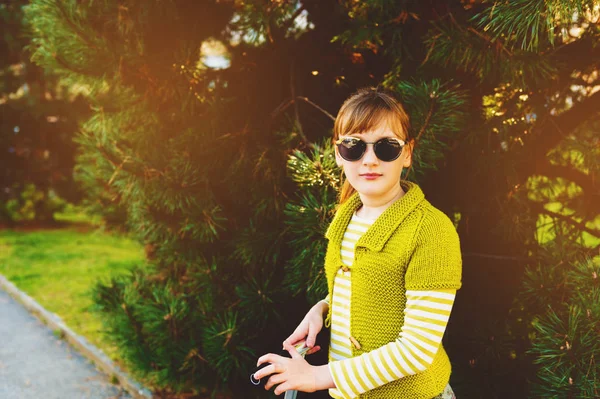 Modeporträt eines niedlichen kleinen Mädchens in leuchtend grüner Strickjacke und Sonnenbrille mit Roller — Stockfoto
