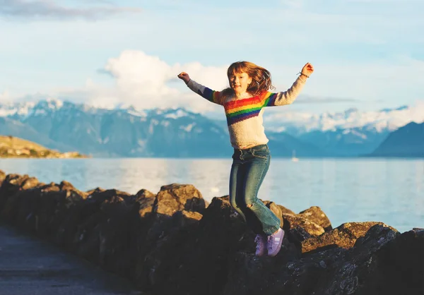 Счастливая и молодая девочка играет рядом с озером Женева на закате, руки широко раскрыты — стоковое фото