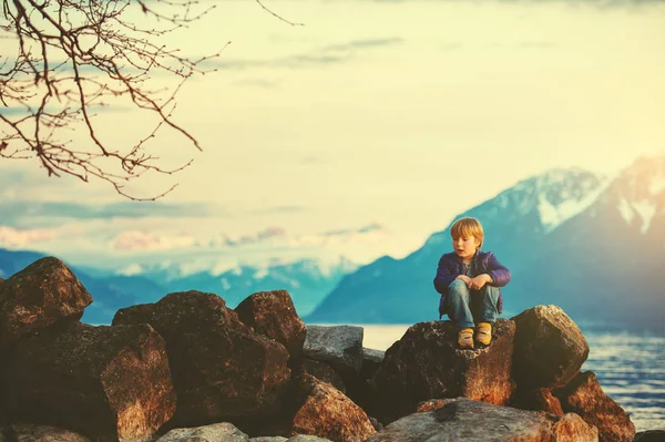 Один счастливый мальчик играет на озере Женева на закате со швейцарскими горами Альпы на заднем плане. Фотография сделана в Лозанне, Швейцария — стоковое фото