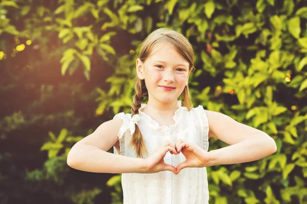 Bambina che fa segno di cuore con le mani nel giardino estivo al tramonto — Foto Stock