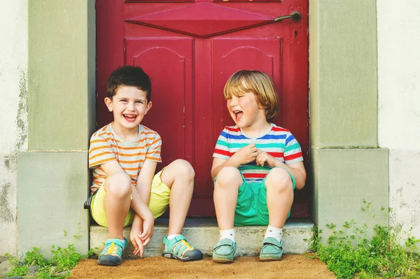 Grupo de dois meninos engraçados brincando juntos ao ar livre, vestindo camisetas coloridas, shorts e sapatos, moda de verão para crianças . — Fotografia de Stock
