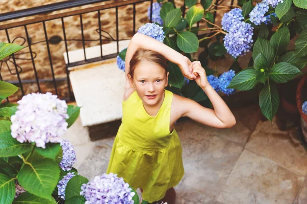 Adorável menina brincando no pequeno jardim hortênsia, vestindo vestido verde verão brilhante, vista superior — Fotografia de Stock