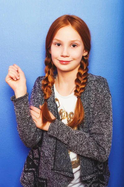 Estudio de toma de bastante preadolescente niña pelirroja de 9-10 años, usando cárdigan gris, de pie sobre fondo azul púrpura —  Fotos de Stock