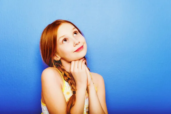 Studio shot of young preteen 9-10 year old rousse girl wearing yellow top, debout sur fond bleu violet, levant les yeux — Photo