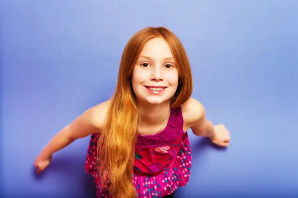 Studio shot of young preteen 9-10 year old redhead girl wearing pink top, standing against blue purple background — Stock Photo, Image