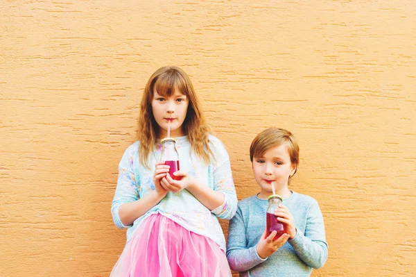 室外肖像的两个有趣时尚孩子，拿着饮料，戴着蓝色和粉红色的衣服 — 图库照片