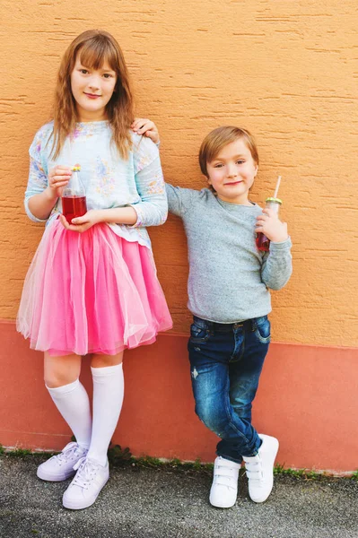 Outdoor Portret van twee grappige mode kinderen, houdt van de dranken, dragen van blauwe en roze kleding — Stockfoto