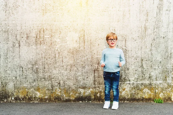 Ritratto all'aperto di un simpatico bambino che indossa occhiali, pullover azzurro e jeans in denim. Concetto di ritorno a scuola — Foto Stock