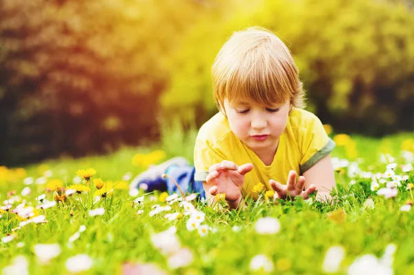 Foto musim panas yang cerah dari anak laki-laki tampan bermain di luar ruangan pada hari yang hangat, berbaring di rumput hijau cerah, mengenakan kaos kuning — Stok Foto