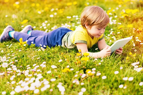 Happy little kid boy playing tablet PC outdoors in the park on a very sunny day — Stock Photo, Image