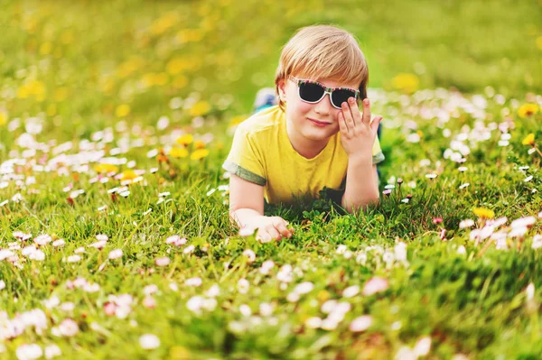 Ritratto estivo soleggiato di giovane bel bambino che gioca all'aperto in una bella giornata calda, sdraiato su erba verde brillante, indossando t-shirt gialla e occhiali da sole — Foto Stock