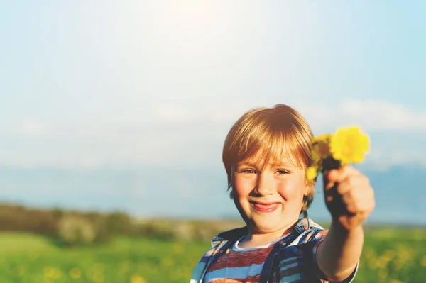 Schattige kleine jongen spelen met bloemen buitenshuis — Stockfoto