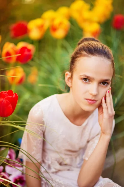 Spring portrait of sweet little girl wearing party dress, sitting outdoors with yellow and red tulips on background — Stock Photo, Image