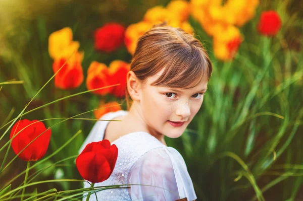 Frühlingsporträt des süßen kleinen Mädchens im Partykleid, im Freien sitzend mit gelben und roten Tulpen auf dem Hintergrund — Stockfoto