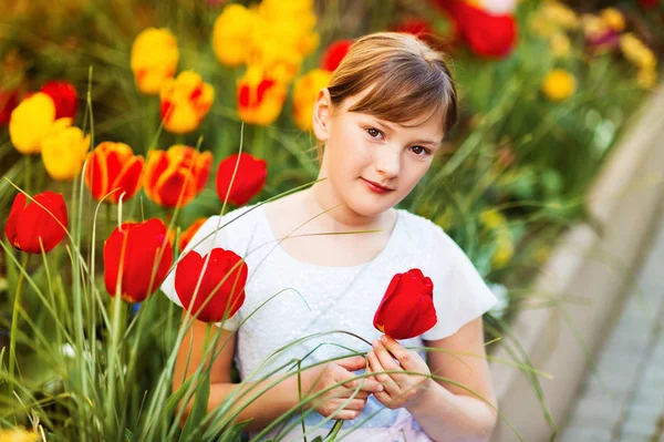 Ritratto primaverile di dolce bambina vestita da festa, seduta all'aperto con tulipani gialli e rossi sullo sfondo — Foto Stock