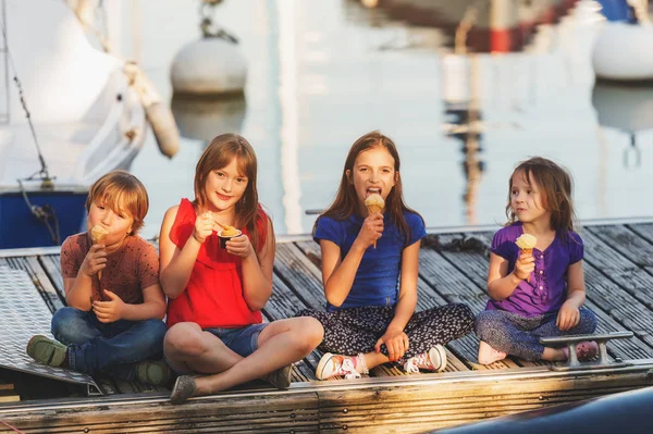 Groep van vier kinderen, 3 meisjes en een jongen, buitenshuis eten van ijs, rustend op een pier bij het meer — Stockfoto