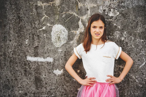 Preteen flicka med tänder hängslen bär vackra klänning, stående mot grå stadsmuren — Stockfoto