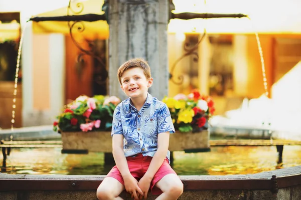 Retrato de verano al aire libre del adorable niño descansando al aire libre junto a la fuente en un día soleado muy caluroso, con camisa estampada azul —  Fotos de Stock