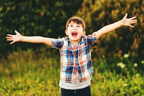 Счастливый мальчик 6 лет развлекается на улице в голубой футболке с широко распростертыми объятиями — стоковое фото