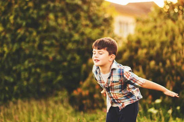 Happy kid boy of 6 year old having fun outdoors wearing blue plaid shirt, pretending to be a plane, eyes closed — Stock Photo, Image